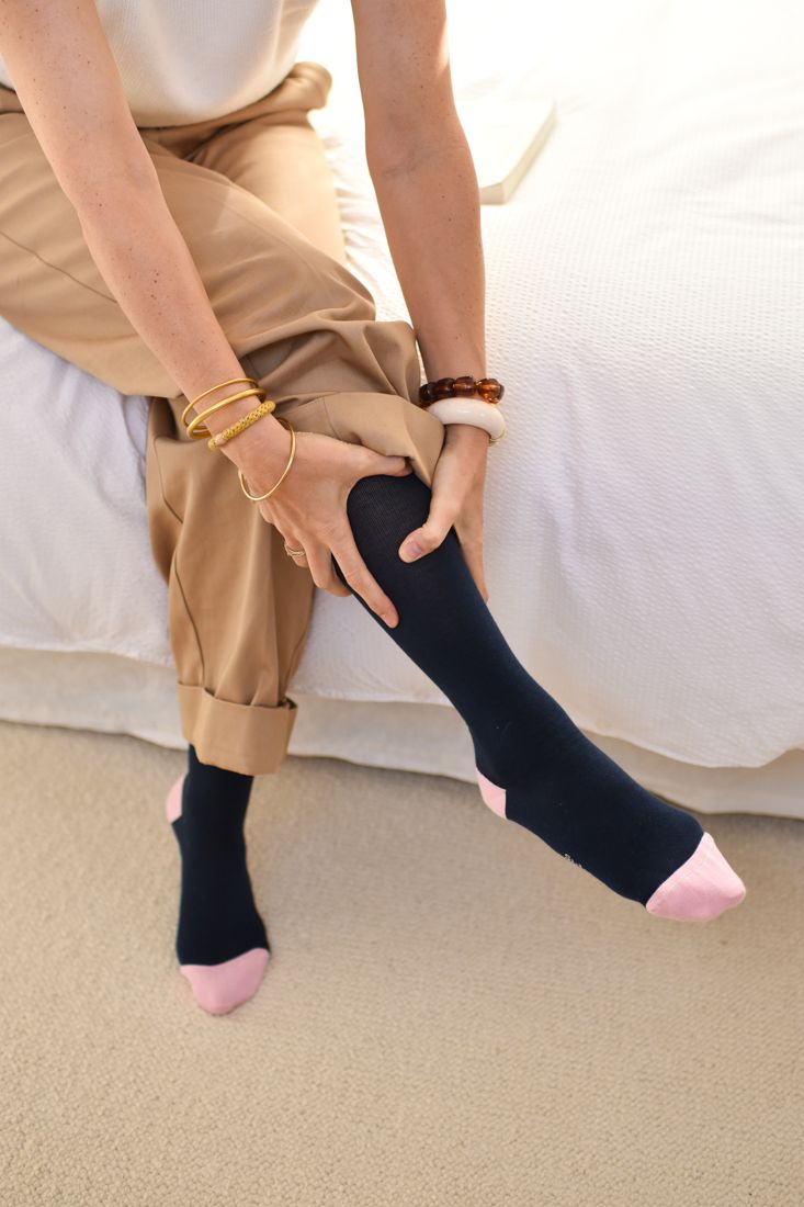 Une femme assise au bord du lit se masse la jambe